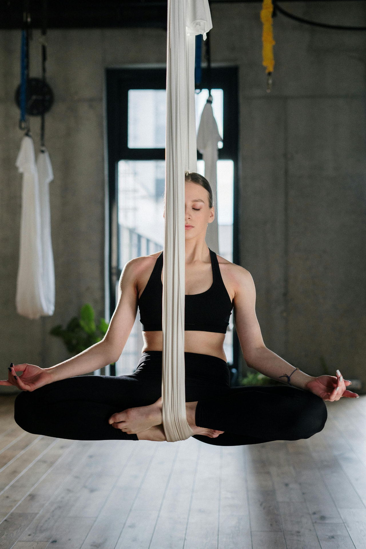 A woman seated in lotus, suspended in an aerial silk. Learning to shift state.