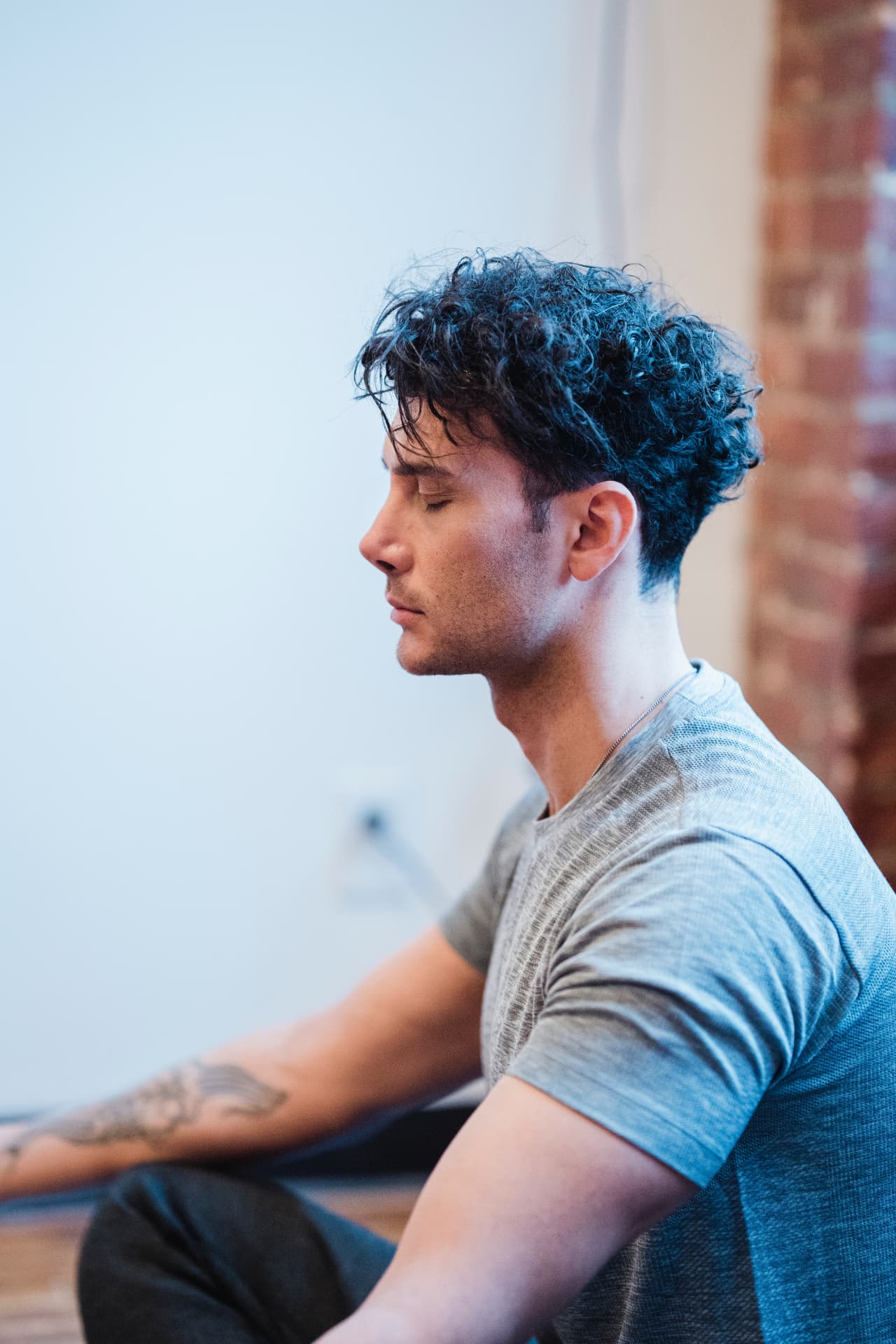 A man seated against a soft wall, eyes closed in quiet meditation. Different lives, the same pattern.