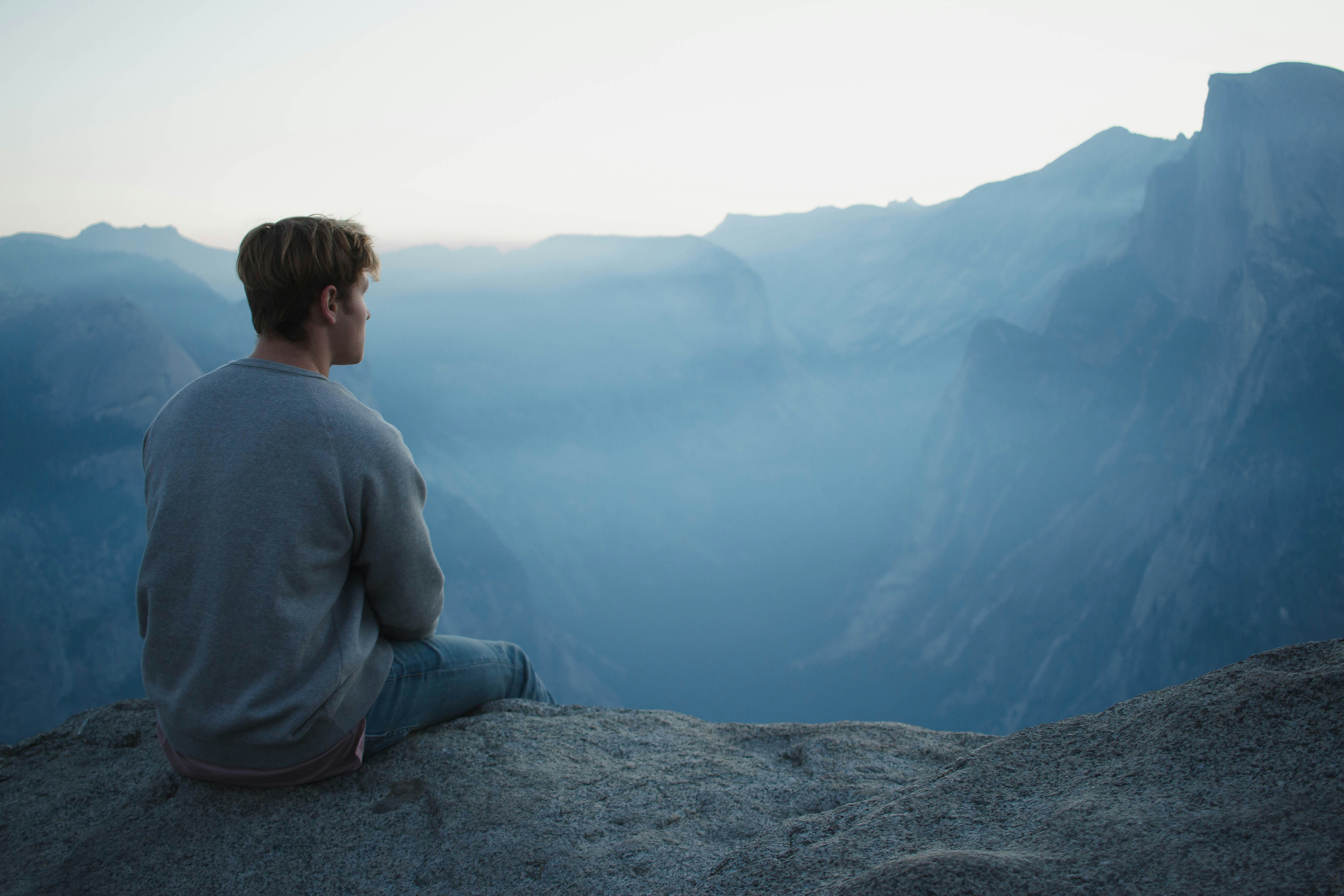 A figure seated at the edge of a vast canyon at first light.