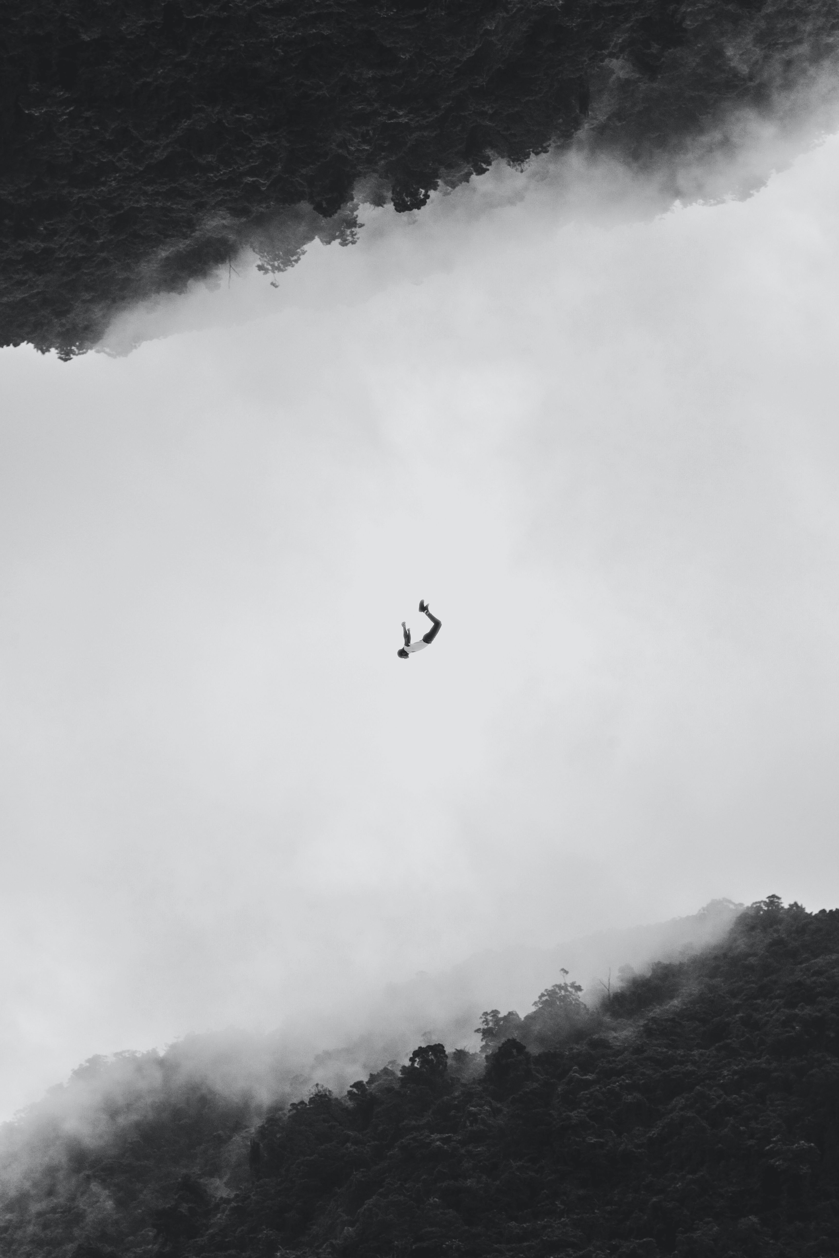 A lone figure suspended mid-air against soft cloud and stone.